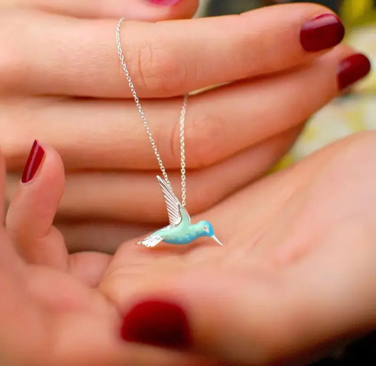 A silver pendant with a blue enamel bird design